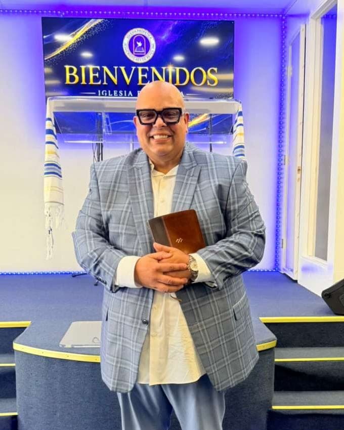 El predicador Ruben Castillo sonriendo con su Biblia frente al altar de la iglesia